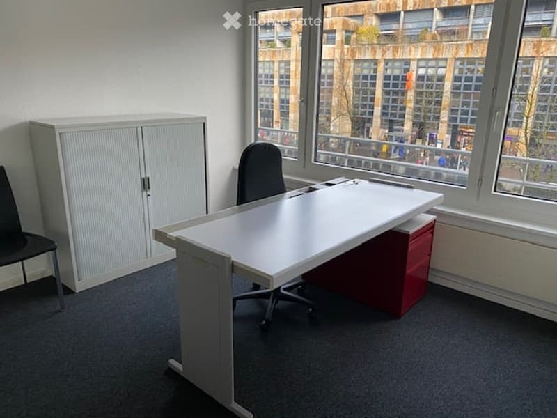 white desk, black chair, white cabinet, red storage box, gray carpet, window with view of city