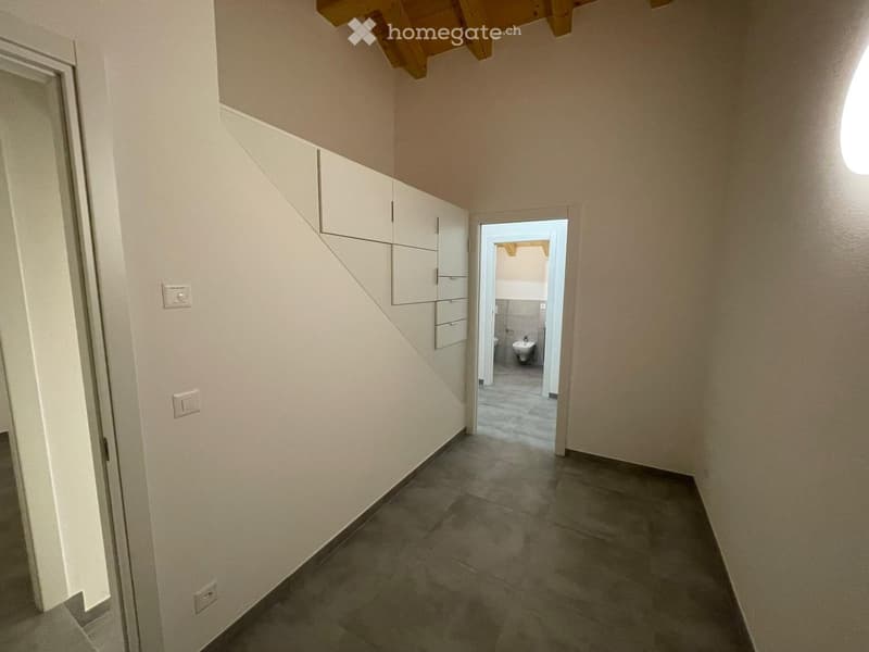 White walls, tiled floor, wooden ceiling, white built-in wardrobes, open door to bathroom