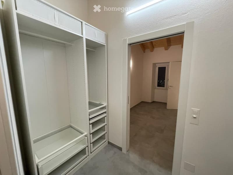 empty walk-in closet with built-in shelves, drawers, and a wooden ceiling beam