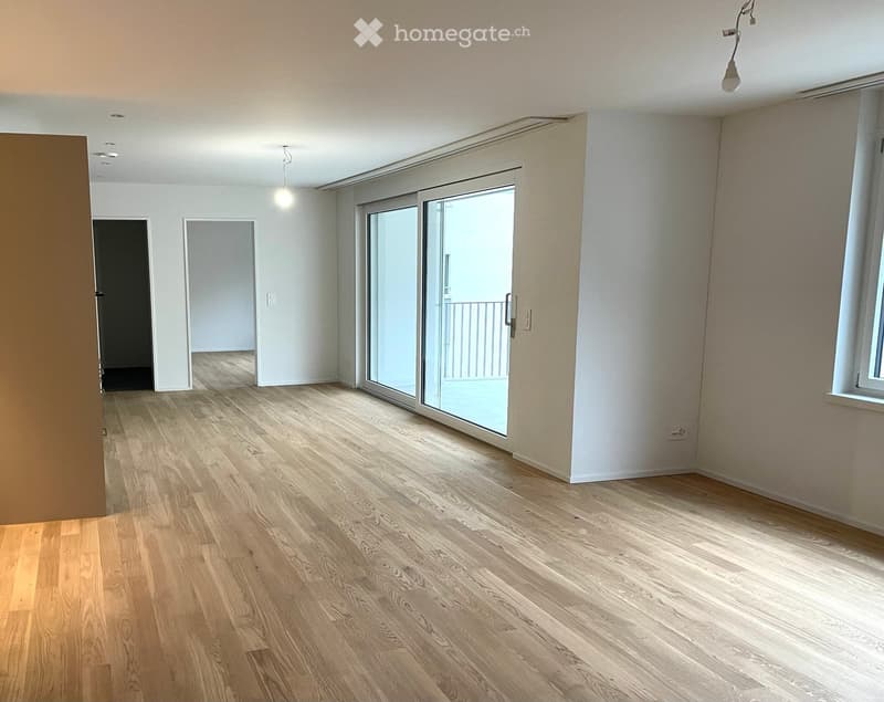 Large open living space with wooden floors, sliding glass door to balcony, and modern decor
