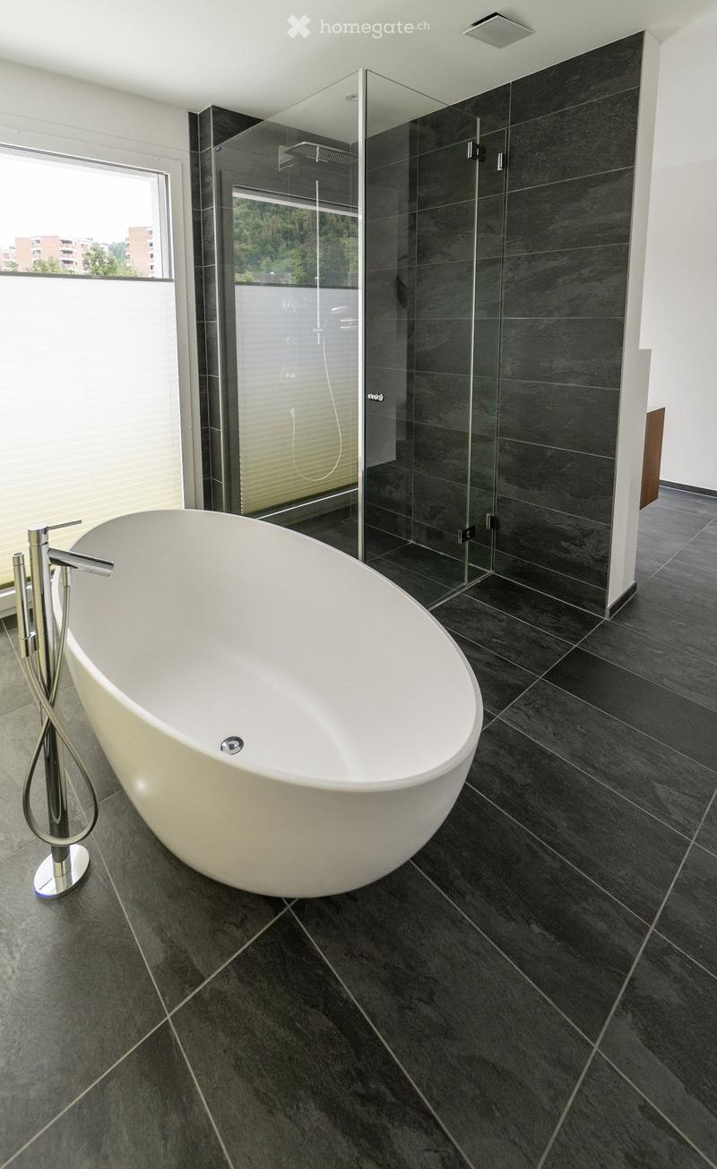 modern bathroom with a large white bathtub, glass shower enclosure, and black tiled floor