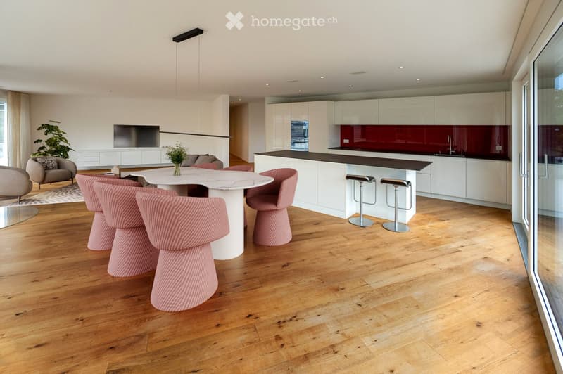 modern open-plan living and dining area with wooden floor, white marble table, pink chairs, white kitchen with red backsplash, glass door leading to balcony