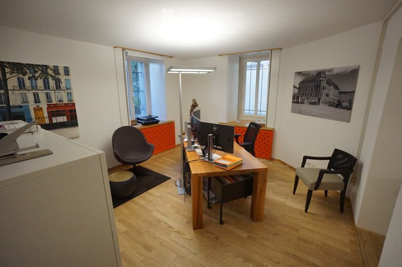 Wooden desk with monitors, black chairs, white cabinet, carpet, paintings on the wall