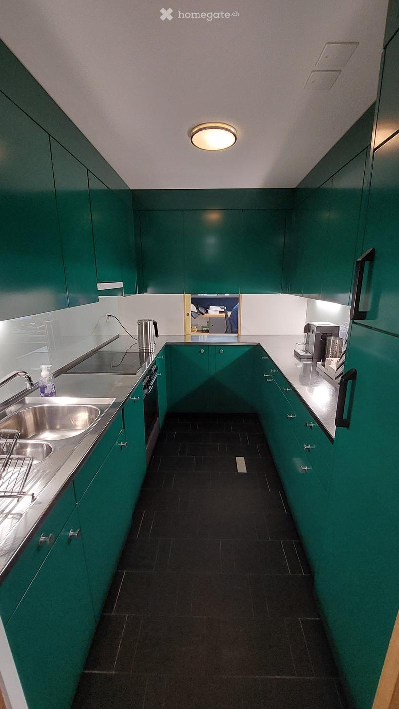 Modern kitchen with green cabinets, tiled floor, large sink, gas stove, and a hanging silver kettle