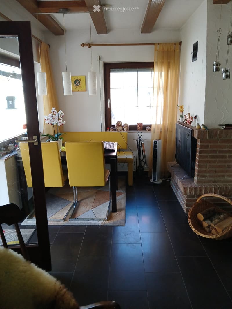 A dining room with yellow chairs, a table, a fireplace, curtains, and a flower vase.