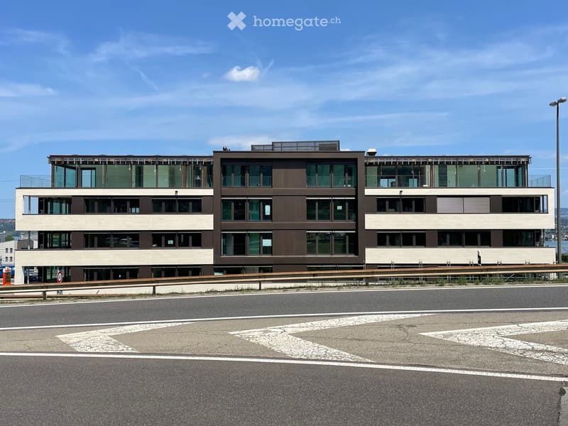Modern three-story building with large windows and a flat roof, situated near a road with clear markings.