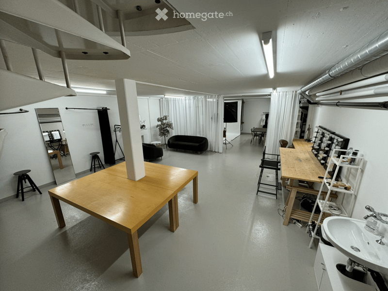 Wide open room with white walls, wooden tables, benches, couch, mirror, plants, ceiling lamps