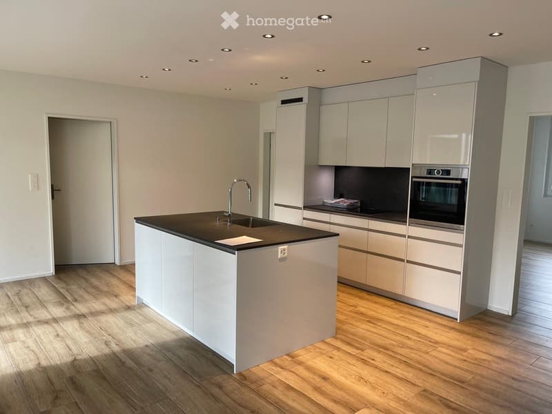 Modern kitchen with white cabinets, a central island, and a black countertop. Features include a sink with a modern faucet, an integrated oven, and recessed ceiling lighting.