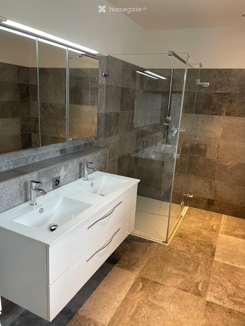 Modern bathroom with a double sink, sleek white cabinetry, a large mirror, and a glass-enclosed shower stall.