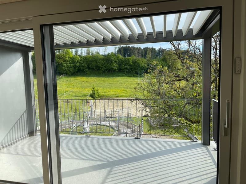 Balcony / Terrace. Modern balcony with large glass doors, white tiled floor, metal railing, and a view of a green field and trees.