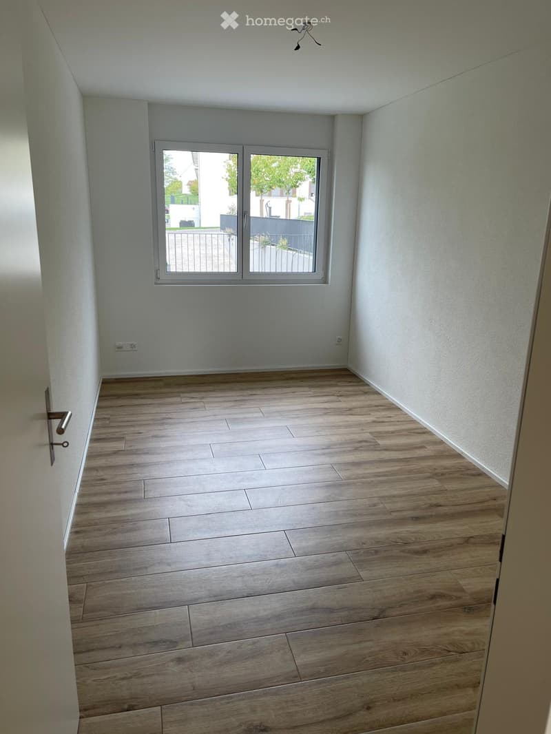Empty room with light wooden flooring, white walls, and a large window with a sliding door leading to an outdoor area.