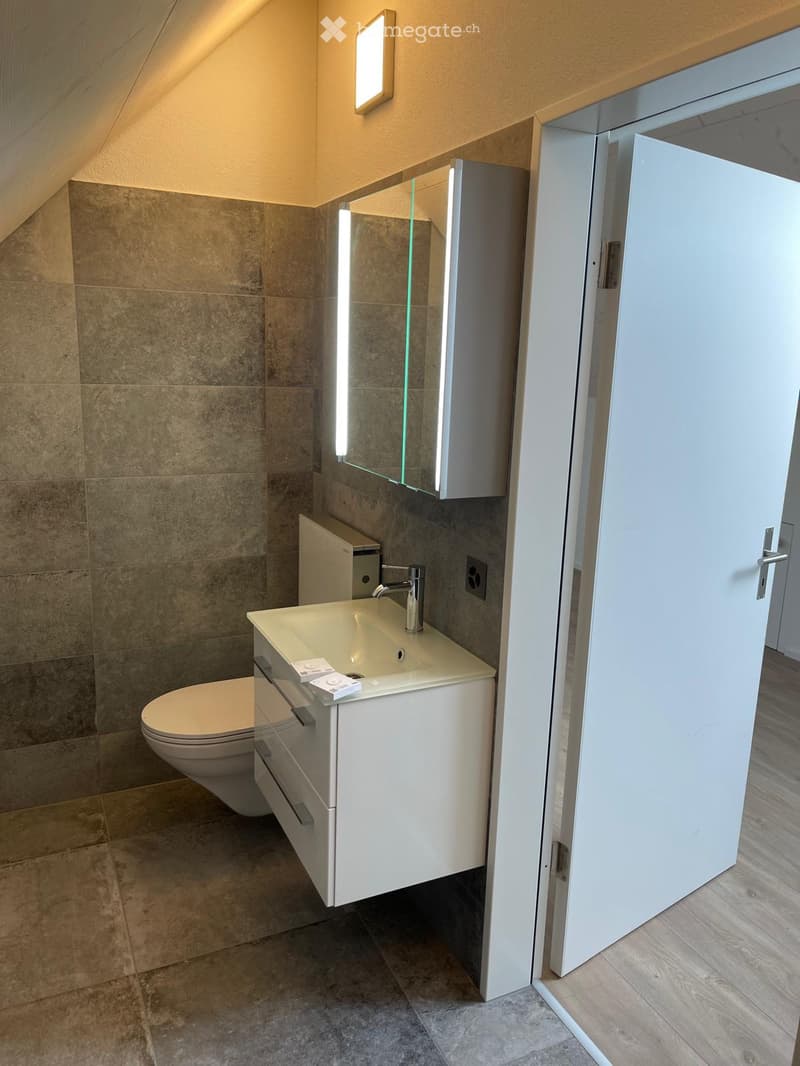 Bathroom. Modern bathroom with beige tiled walls, a white sink with a chrome faucet, a toilet, and a mirrored cabinet with built-in lighting.