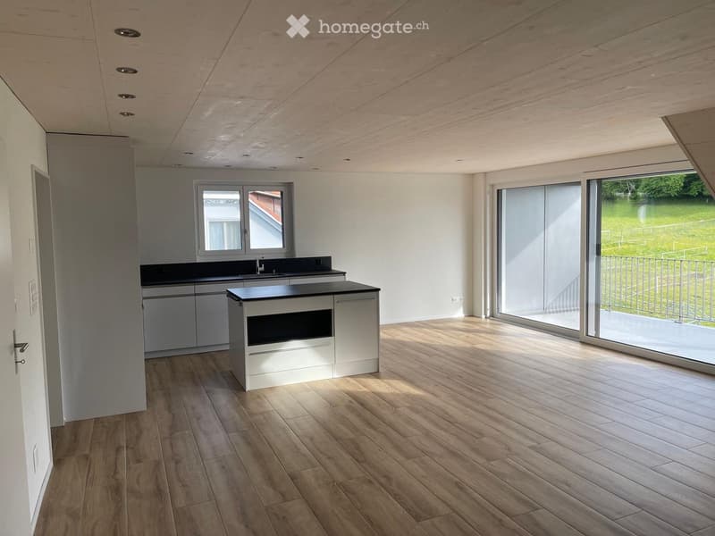 Kitchen. Modern kitchen with light wood flooring, white cabinets, and a central island with an oven. Large windows and sliding glass doors lead to a balcony.