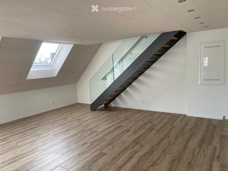 Unfurnished Room. Empty room with wooden flooring, white walls, and a modern staircase with glass railing leading to a loft area. Skylight window provides natural light.