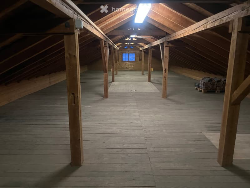 Empty attic with wooden beams, wooden floor, fluorescent lights, and a small window