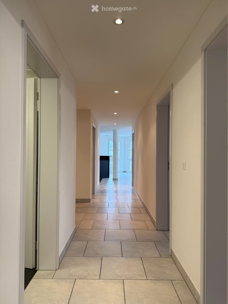 Corridor / Hallway. Clean, modern hallway with tiled flooring, beige walls, and recessed lighting. Doors on both sides lead to other rooms.