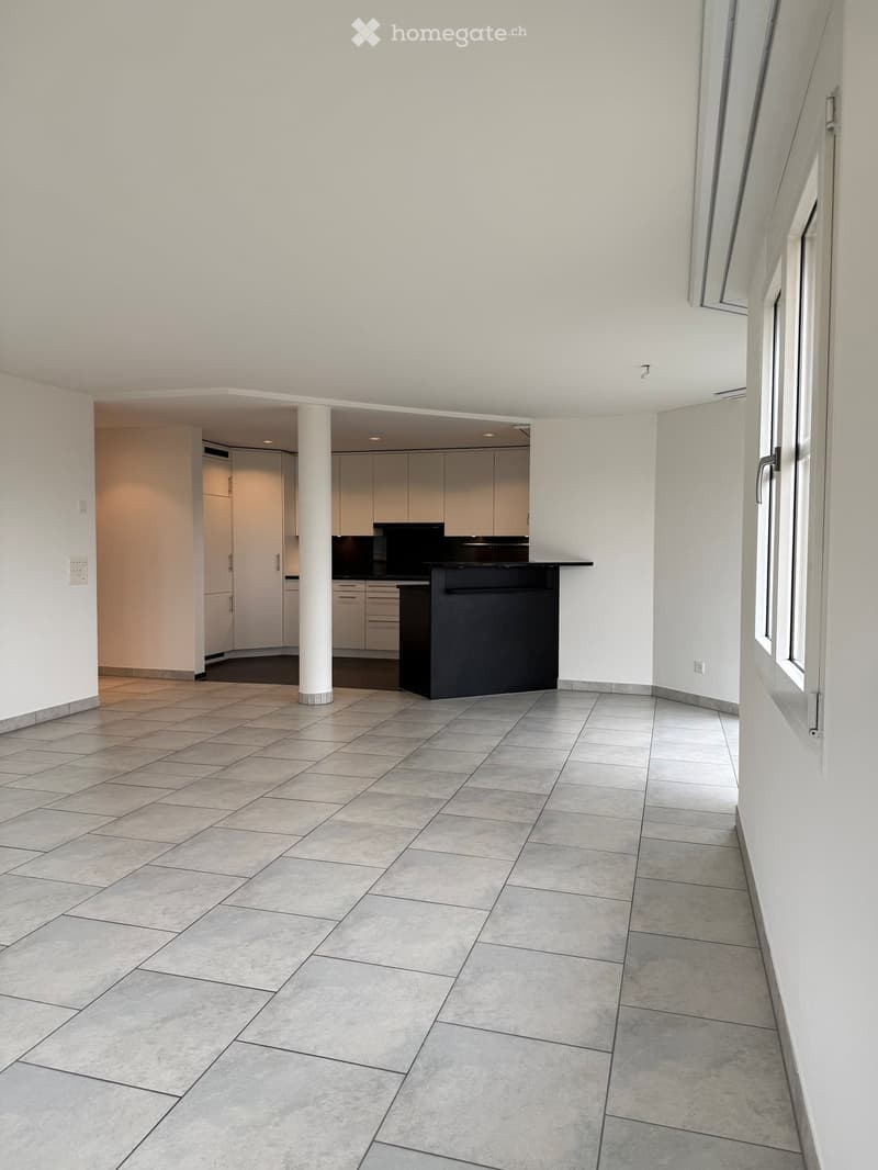 Unfurnished Room. Empty room with tiled floor, white walls, and a central column. A small kitchen area is visible in the background with cabinets and a countertop.
