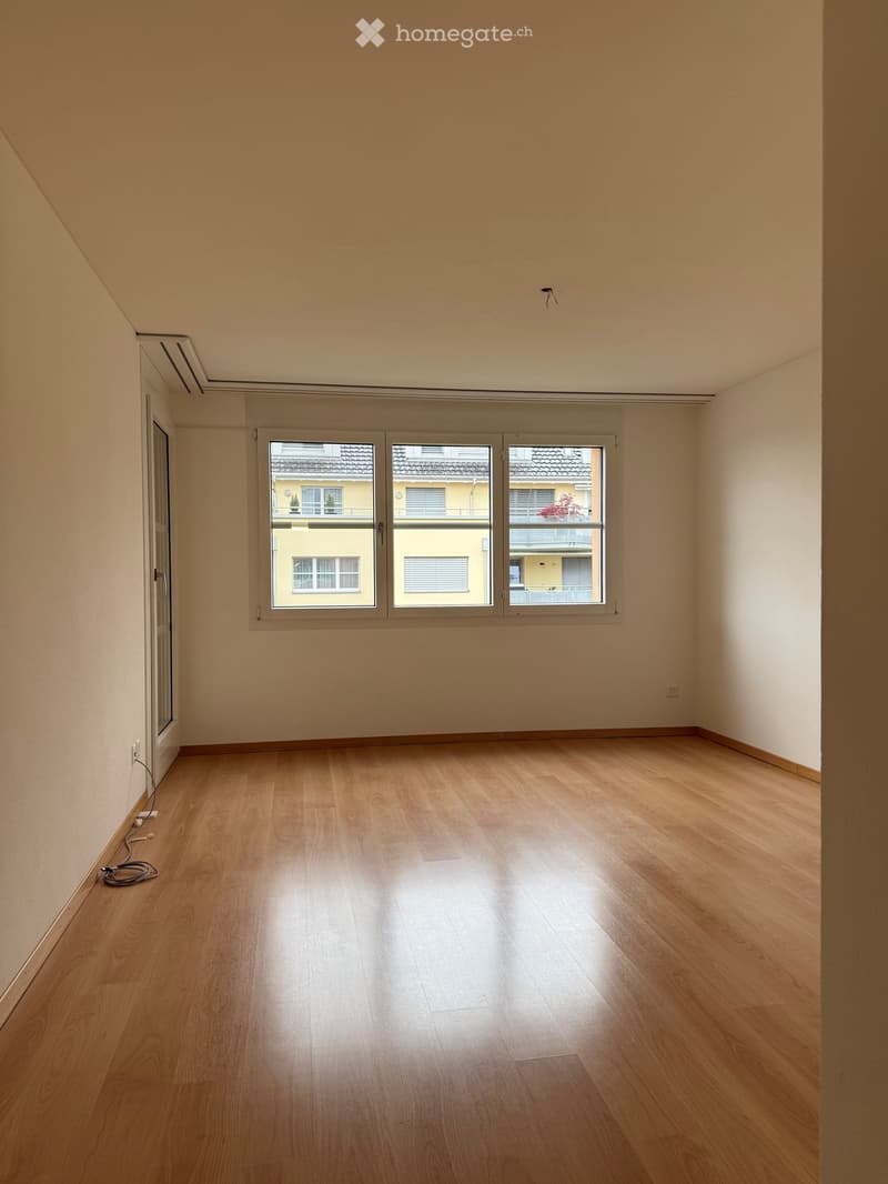 Unfurnished Room. Empty room with light wooden flooring and large windows showing a view of neighboring buildings.