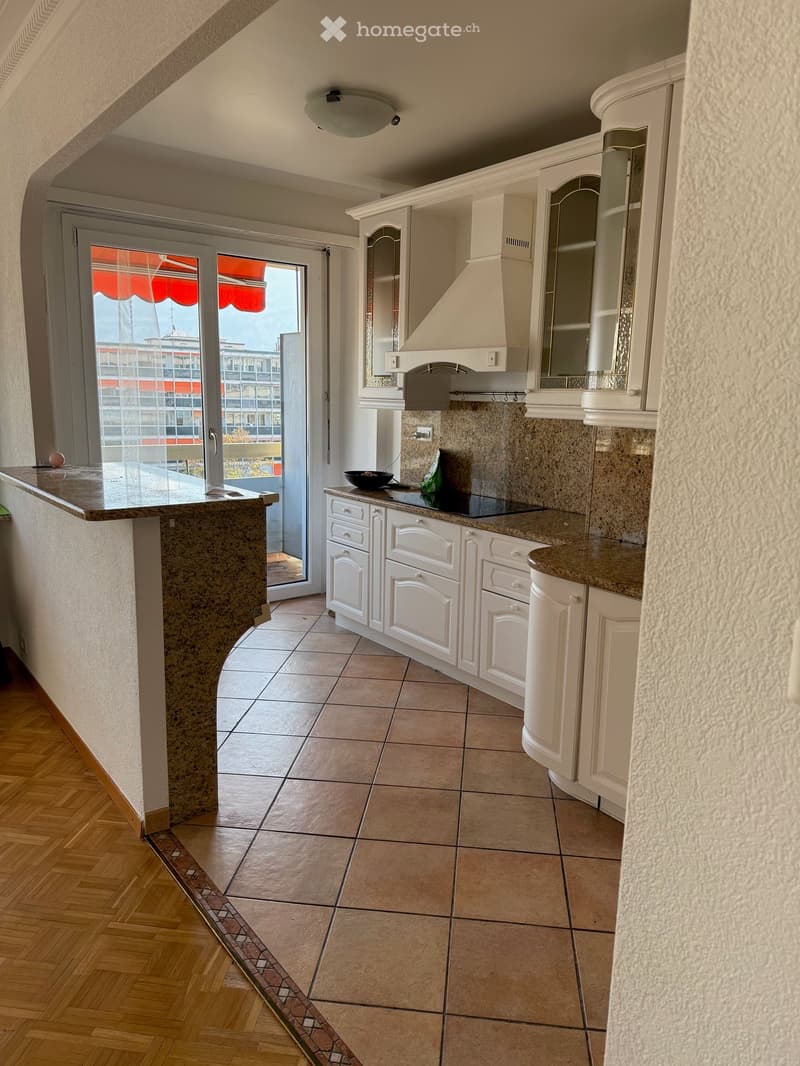 open kitchen with large island, white cabinets, marble countertops, stainless steel appliance, sliding glass doors to balcony