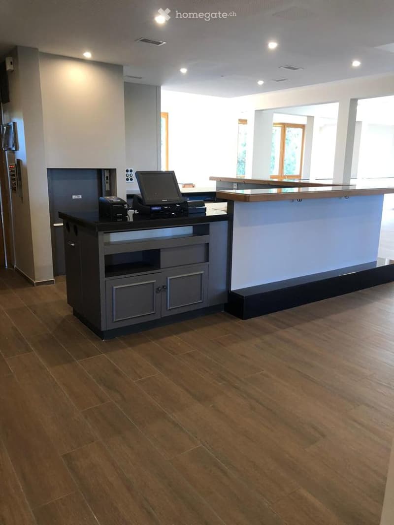 Reception area with wood flooring, grey desk, black countertop, monitor, black printer, wooden desk with drawers