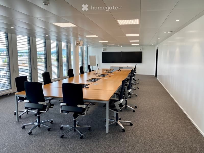 Conference room with a long wooden table, multiple chairs, and a large screen at the back.