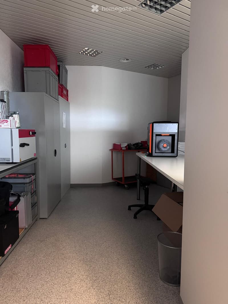 empty room with cabinet, storage boxes, desk with computer, cart, and trash bin
