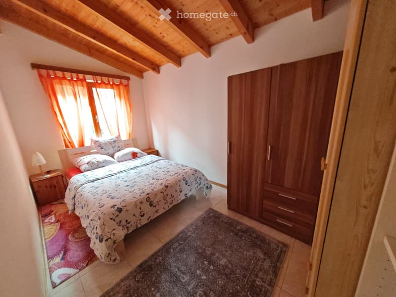 A bedroom with a bed, side tables, lamps, wooden cabinet, rug, and a window with curtains.