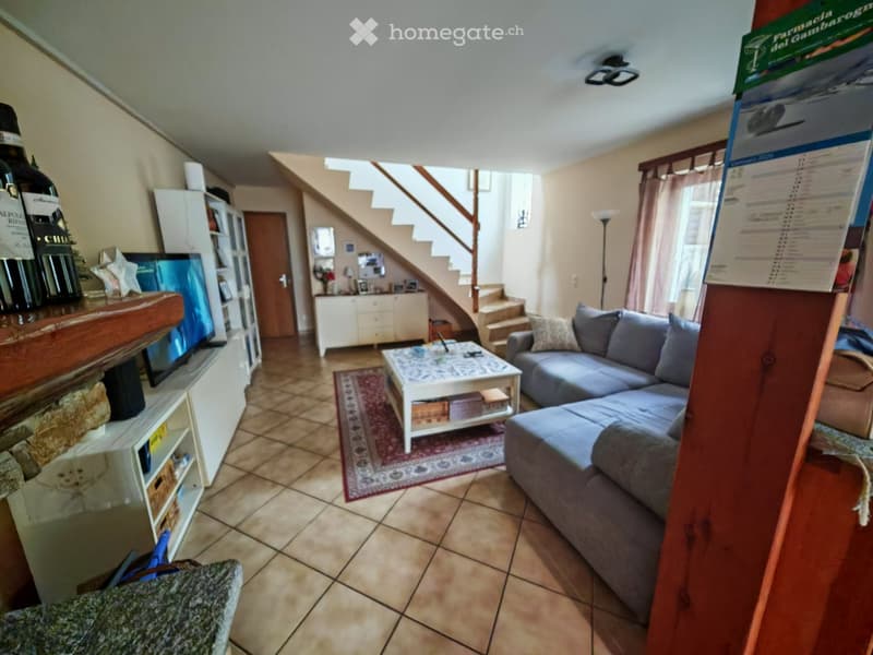 Living room: two gray sofas, white coffee table, white cabinets, blue TV, rug, staircase, fireplace