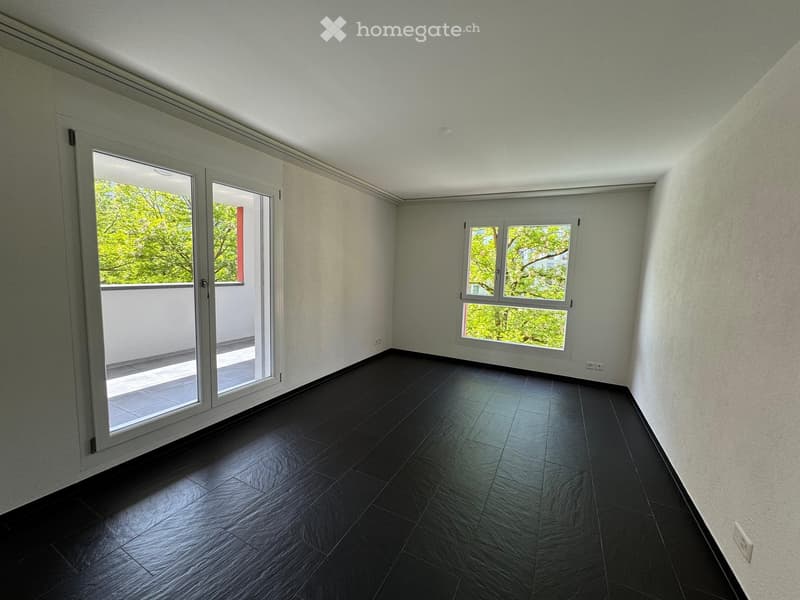 Empty room with dark tiled flooring, white walls, large windows, and a sliding glass door leading to a balcony.