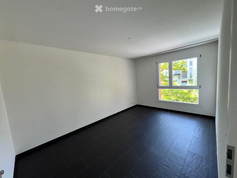 Empty room with white walls, dark tiled floor, and large window with blinds.