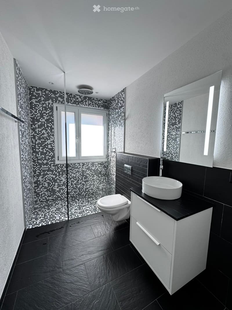 Modern bathroom with black and white tiles, a toilet, a sink with a mirror, and a window providing natural light.