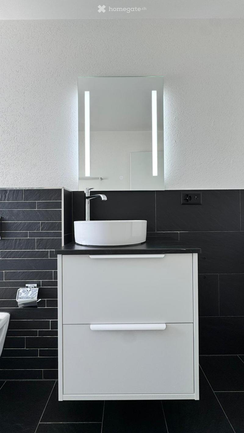 Modern bathroom with a sleek white sink, chrome faucet, illuminated mirror, and a white cabinet with two drawers.