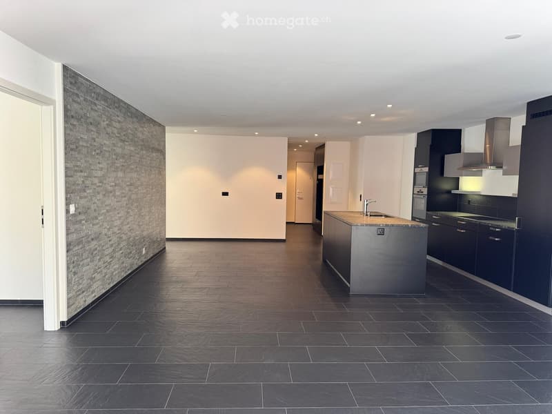 Modern kitchen with dark tiled floor, grey brick accent wall, kitchen island with sink, and dark cabinets.