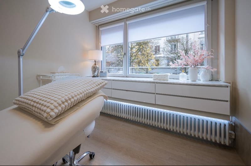 A beauty treatment room with massage table, a lamp, and a heater under a large window.