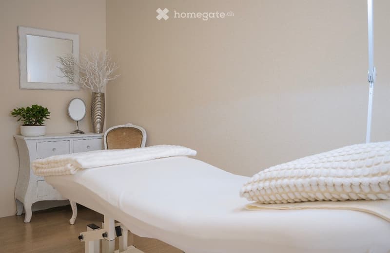 treatment room with massage table, mirror, cabinet with potted plant, chair, and decorative vase