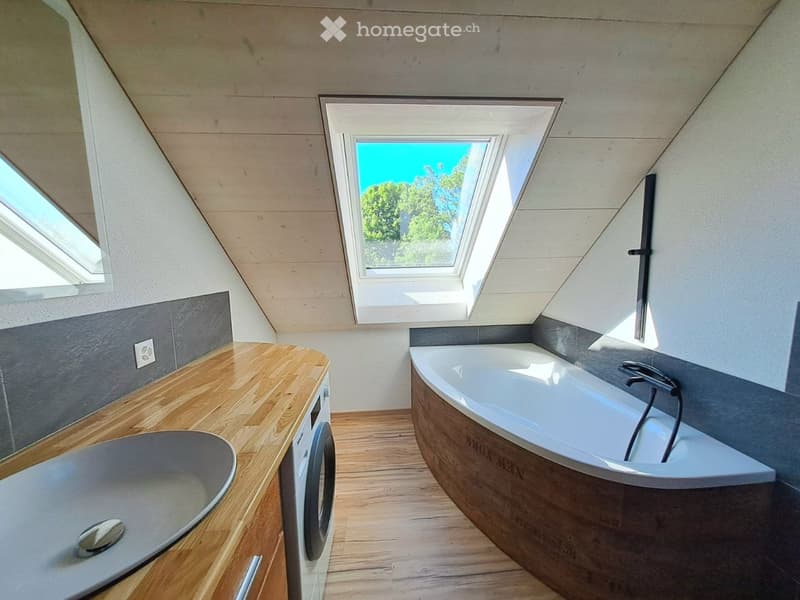 Bathroom. Modern bathroom with a wooden countertop, a bathtub, a sink, and a washing machine. The room features skylight windows and wooden flooring.