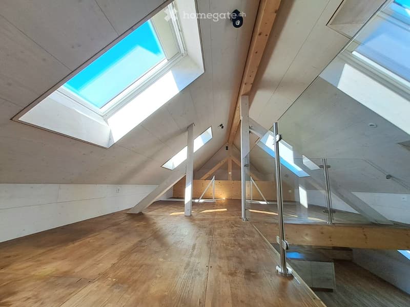 Unfurnished Room. Empty attic space with wooden flooring, exposed wooden beams, and skylights allowing natural light to fill the room. A glass staircase leads to another level.