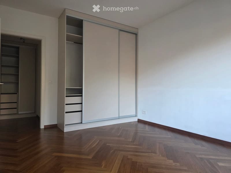 empty room with wooden floor, white walls, two wardrobes with drawers, and an open door to another room