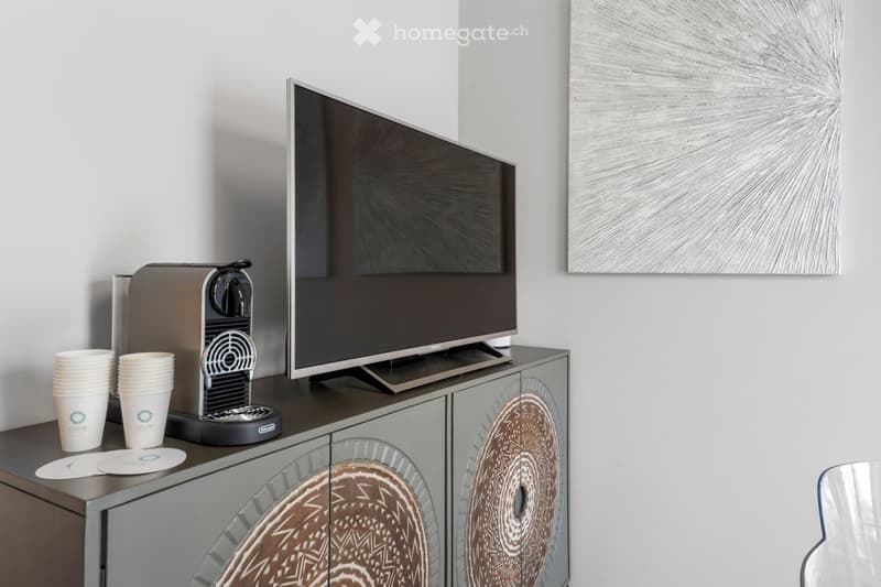 A cabinet, a flat screen TV, a coffee machine, two paper cups, two coasters, a painting, a chair