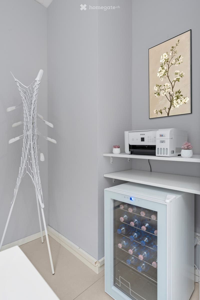 A small room with a clothes rack, a desk, a printer, and a wine cooler.