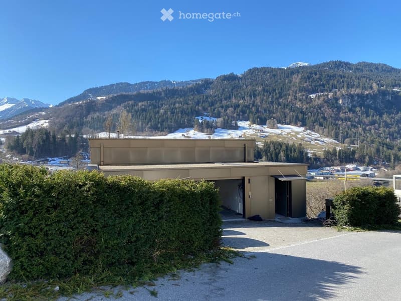 Building with a garage, mountain in the background, and an open area in front