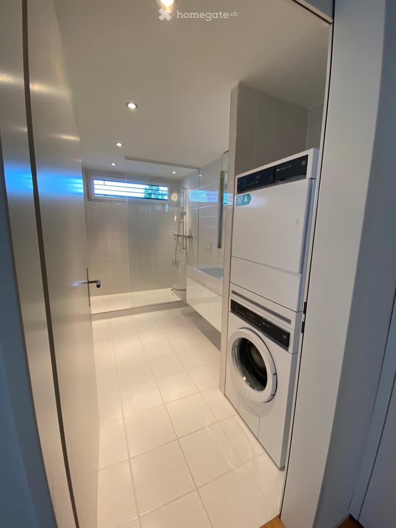 Modern bathroom, white tiles, glass door, toilet, sink, washing machine, dryer