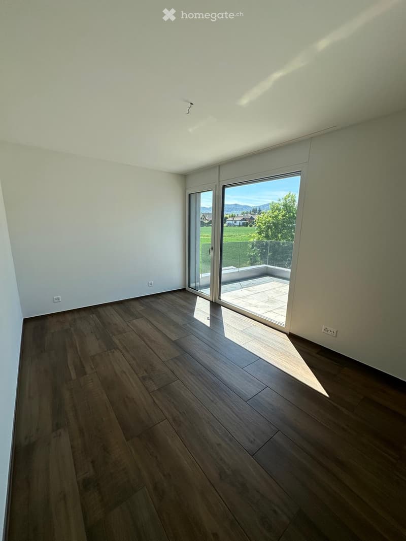 Empty room with wooden flooring, white walls, and large sliding glass doors leading to a balcony with a scenic view.