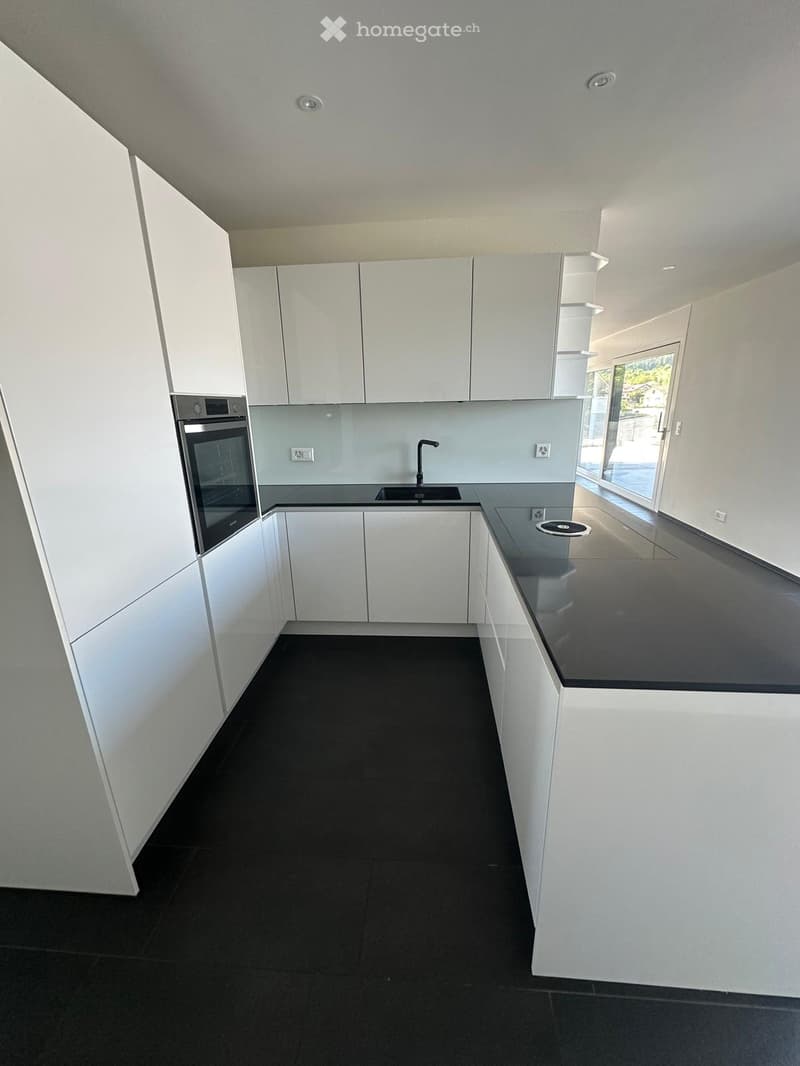Modern, minimalist kitchen with white cabinets, black countertops, and a black tiled floor. Features an integrated oven and a sink with a modern faucet.