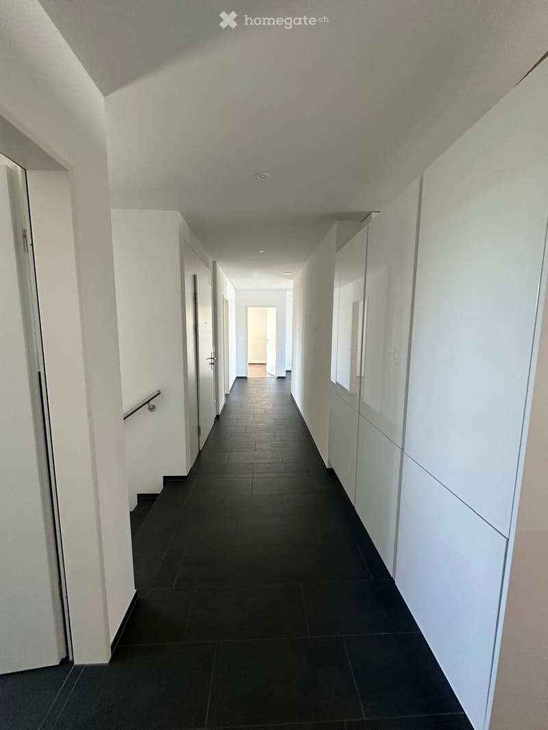Clean, modern hallway with black tiled flooring, white walls, and several doors on both sides. A handrail is visible on the left side.