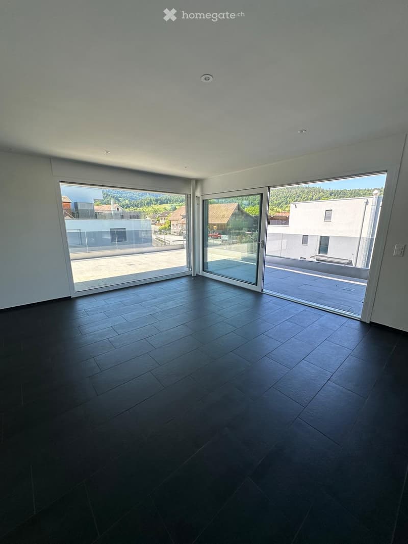 Empty room with dark tiled floor, large glass sliding doors leading to a balcony, and white walls.