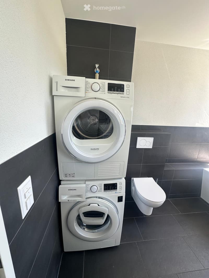 Modern bathroom with a stacked Samsung washing machine and dryer, and a white toilet.