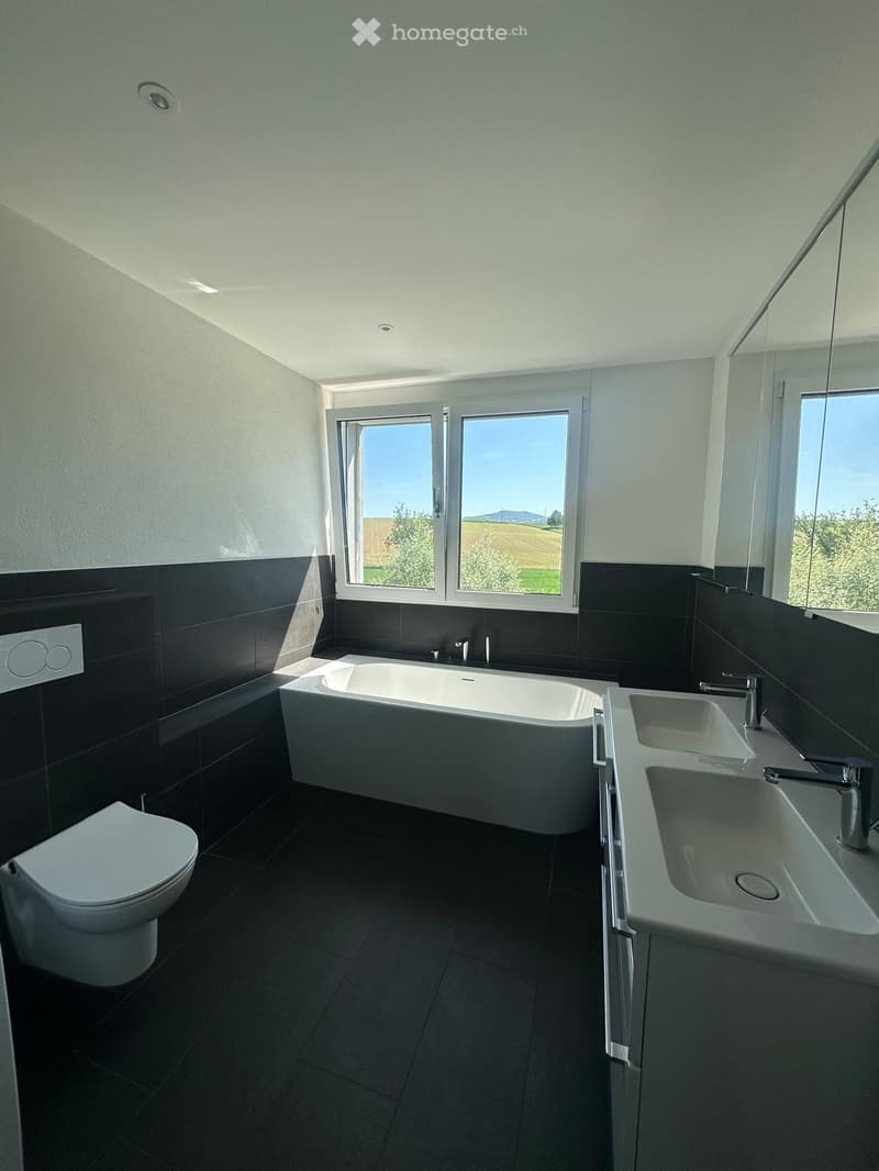 Modern bathroom with a bathtub, toilet, sink, and large windows offering a scenic view.