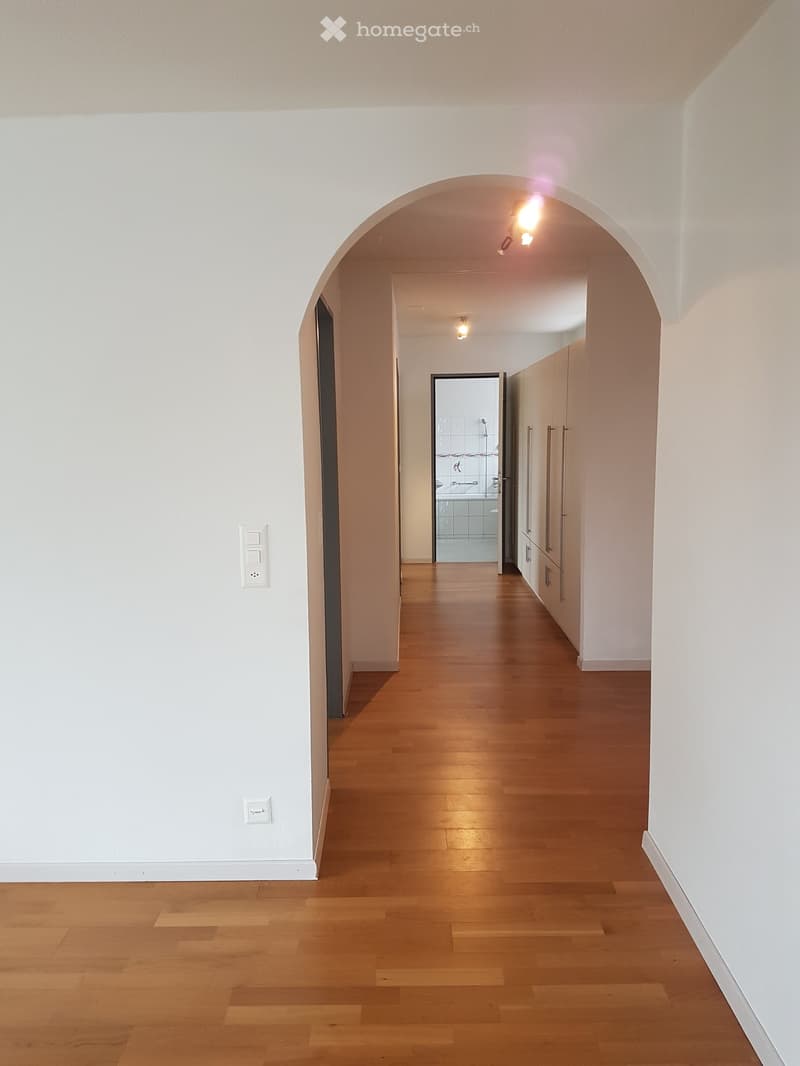 Empty hallway with wooden floor, white walls, arched ceiling, and doors leading to other rooms