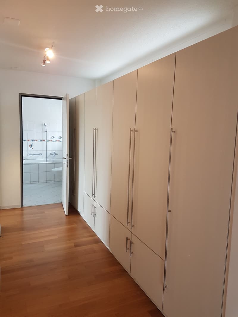 wooden floor, white walls, large white cabinets, open door to bathroom